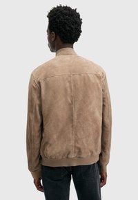 Giubbotto bomber in suede color marrone chiaro con colletto e polsini a costine, caratterizzato da una texture liscia e da un design minimalista.