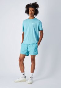 Vaaleansininen t-paita ja yhdessä sopivat shortsit hengittävästä kankaasta. Varustettu logoyksityiskohdilla ja rennolla istuvuudella. Yhdistetty valkoisiin lenkkareihin ja sukkiin.