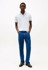 Polo di colore azzurro con colletto, abbinato a jeans di denim blu. I jeans hanno una vestibilità dritta. Scarpe nere completano l'outfit.