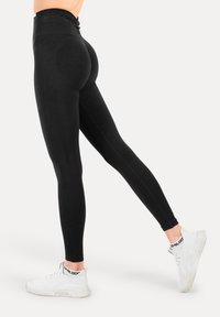 Czarne legginsy z wysokim stanem o gładkiej fakturze, z dopasowanym krojem i przeszyciami, zestawione z białymi butami sportowymi.