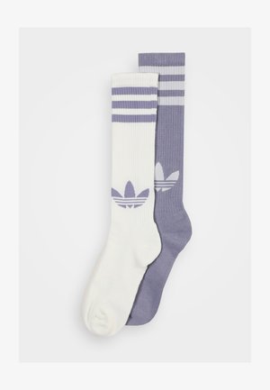 Dwie pary skarpetek: jedna biała z jasnofioletowymi paskami i logo, a druga jasnofioletowa z białymi paskami i logo. Tekstura rybia.