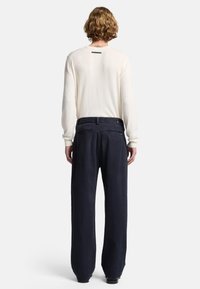 Maglione lungo crema con maniche lunghe e scollatura rotonda, abbinato a pantaloni blu scuro a vestibilità ampia con una finitura leggermente strutturata e tasche posteriori.
