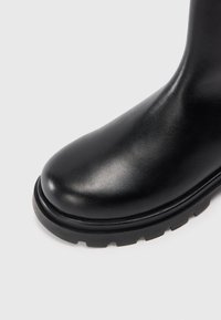 Bottine en cuir noir avec un bout arrondi, une finition lisse et une épaisse semelle en caoutchouc présentant un motif cranté pour une meilleure adhérence.