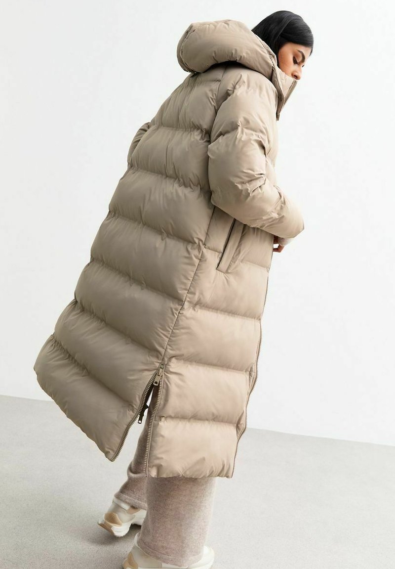 Długa kurtka puchowa w kolorze khaki, z kapturem, pikowanym wzorem, bocznymi kieszeniami i dwukierunkowym zamkiem błyskawicznym dla regulowanego dopasowania.