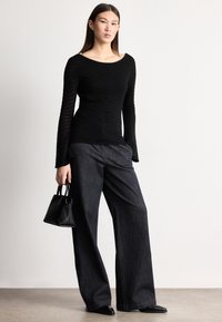 Fekete bordázott hosszú ujjú felső széles nyakkivágással, laza sötét farmernadrággal és egy kis fekete kézitáskával párosítva.