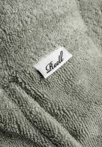 Light gray textured towel with a soft, plush finish; features a sewn white label with black cursive text reading "Reell."