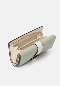 Portefeuille en cuir texturé vert avec des accents crème, comportant plusieurs compartiments et un détail de fermeture éclair dorée. Le design ouvert montre la disposition intérieure.