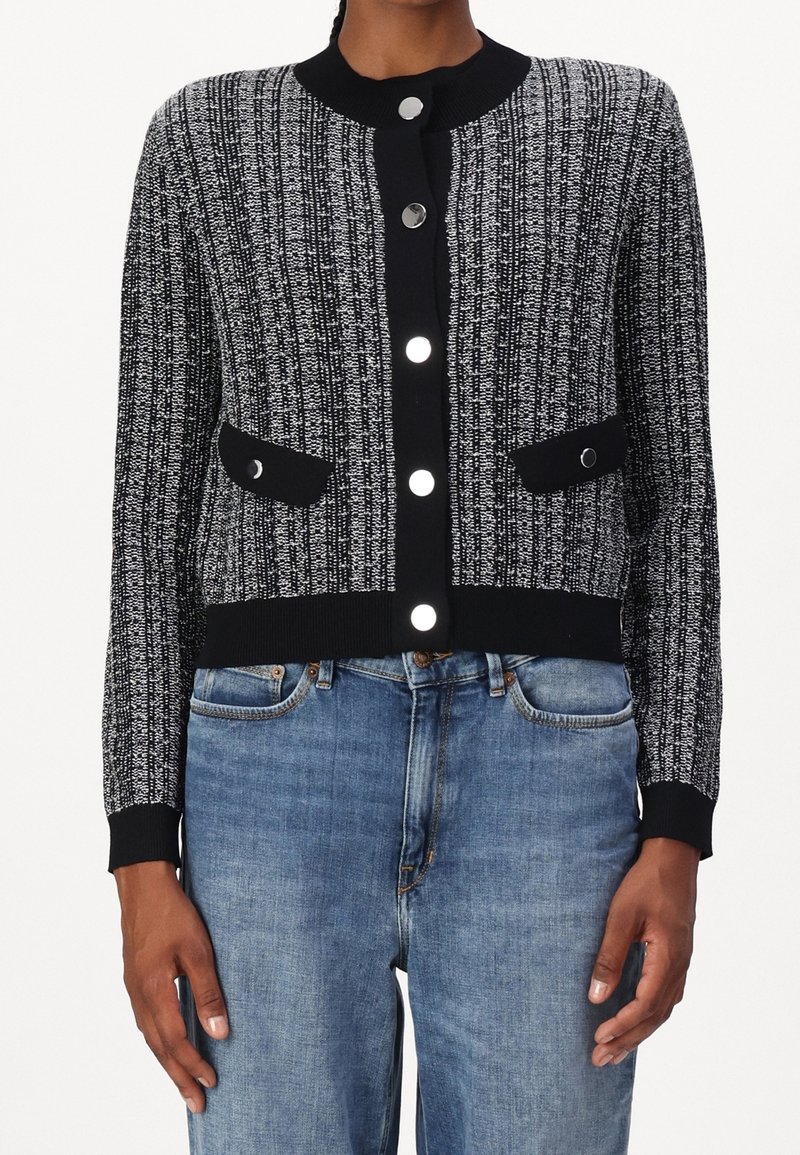 Svart och vit mönstrad kofta med rund halsringning, knäppning med knappar, två framfickor och ribbad ärm. Matchad med ljusblå jeans.