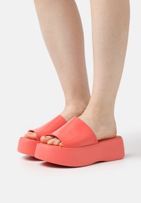 Korallfärgade plattformsandaler med öppen tå-design, tillverkade av glänsande material, med en tjock sula och mjuk textur.