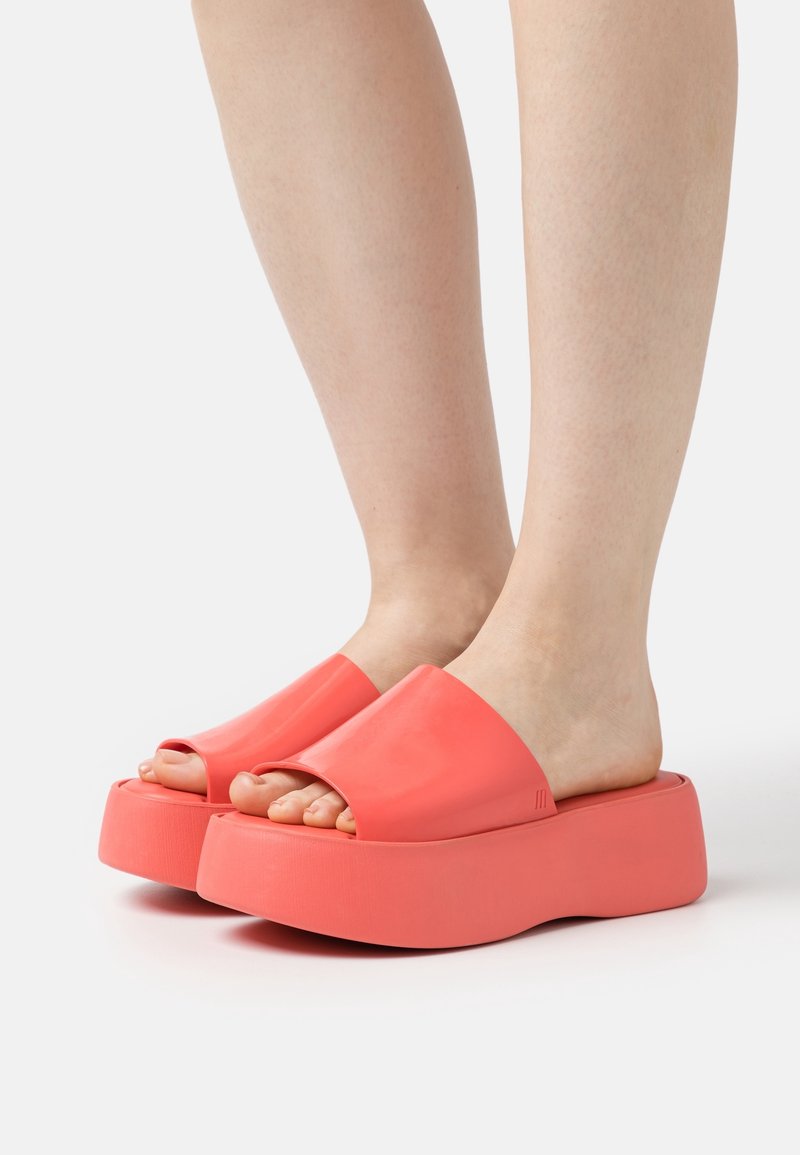 Korallfärgade plattformsandaler med öppen tå-design, tillverkade av glänsande material, med en tjock sula och mjuk textur.