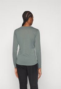 Long-sleeve shirt in muted green fabric, featuring a crew neck and a fitted silhouette, shown from the back with black pants.