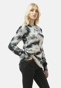 Knit sweater featuring a black and white tie-dye pattern, long sleeves with frayed cuffs, and a ribbed neckline, paired with dark jeans.