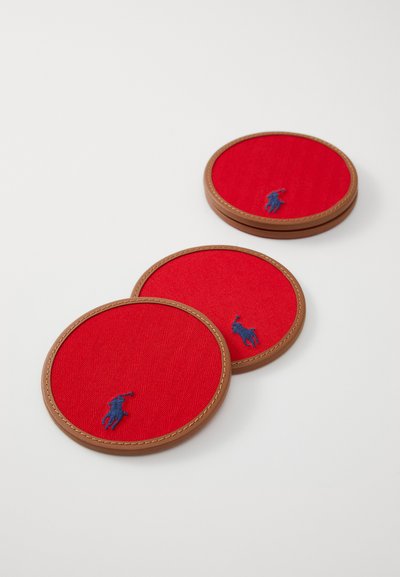 Punased ringikujulised aluspadjad kalasabatekstuuriga, pruunist nahast äärtega, millel on väike sinine tikitud logo. Kolm tükki on välja pandud.