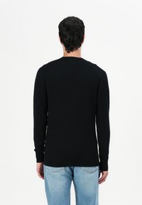 Suéter preto de manga longa com gola redonda, punhos ajustados e uma textura suave, combinado com jeans de tom azul claro.