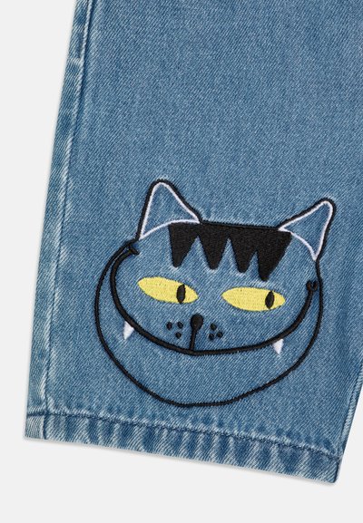 Blå denimtyg med en broderad kattansikte med gula ögon, svarta ränder och vita hängande tänder. Rena kanter och slät textur.