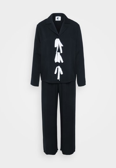 Čierny dvojdielny outfit s blúzkou na golier a bielymi stužkami na prednej strane, doplnený voľnými nohavicami.