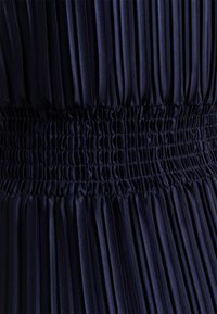 Marinblå plisserad klänning med smockat midjeband, med vertikala veck och en mjuk yta, som framhäver den strukturerade designen och tygkvaliteten.