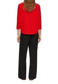 Haut rouge à manches trois-quarts avec un ourlet arrondi, associé à un pantalon évasé noir en matériau doux, vu de dos.