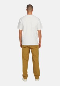 Weißes Baumwoll-T-Shirt mit Rundhalsausschnitt und kurzen Ärmeln, kombiniert mit braunen Hosen. Minimalistisches Design mit lässiger Passform.