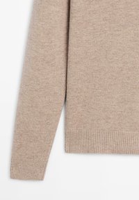 Maglione a pullover beige in maglia con orlo e polsini a coste. La texture del tessuto è morbida e liscia, con un motivo leggermente screziato.