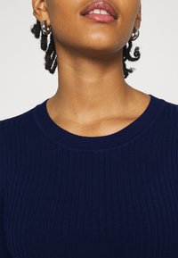 Top a coste navy con scollo rotondo, caratterizzato da una texture morbida e una silhouette aderente, che mette in evidenza l'elasticità e il motivo del tessuto.