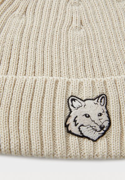 Căciulă tricotată bej, cu un design texturat din dungi. Prezintă o broderie cu fața unei vulpi pe față. Material moale, cu o potrivire strânsă.