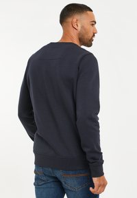 Marine Sweatshirt mit Rundhalsausschnitt und gerippten Bündchen. Verfügt über einen strukturierten Rückensteg und ein weiches Baumwollmischgewebe. Kombiniert mit blauen Jeans.