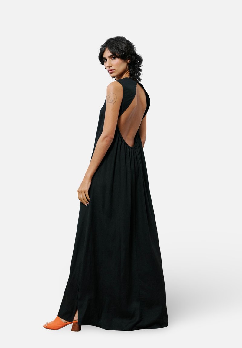 Schwarzes ärmelloses Kleid mit einem tiefen Rückenausschnitt, fließender Textur und Knöchellänge. Es verfügt über eine subtile Raffung an der Taille und einen Seitenschlitz.