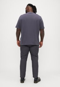 Graues Kurzarm-T-Shirt und dunkelgraue Cargo-Hosen. Das T-Shirt hat einen Rundhalsausschnitt; die Hose ist mit Seitentaschen und einer schmalen Passform ausgestattet. Schwarze Schuhe.