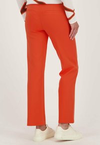 Oranje broek met een rechte snit, gemaakt van een soepele stof. Beschikt over twee achterzakken en gedragen met witte sneakers.