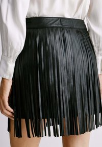 Zwarte leren rok met verticale franjes, een gladde tailleband met stiksels en een label op de achterkant.