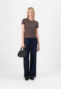Brun, åtsittande t-shirt med kort ärm i kombination med lösa, mörkblå denimbyxor. Håller en liten svart handväska med texturerade detaljer.