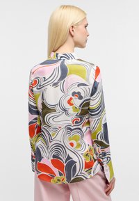 Camicia a maniche lunghe con un motivo floreale colorato e vorticoso in rosa, verde, rosso e blu su uno sfondo bianco. Tessuto morbido, dettagli con bottoni.