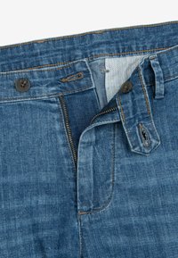 Vaqueros de mezclilla azul con cremallera bajada y cinturilla desabrochada que muestran costuras superiores y patrón del tejido interior.