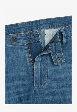 Blaue Denim-Jeans mit geöffnetem Reißverschluss und aufgeknöpftem Bund, die obere Nähte und das Innenstoffmuster sichtbar zeigen.