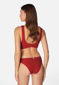 Röd texturerad bikiniuppsättning med en kortärmad topp med breda remmar och låg rygg, i kombination med matchande högmidjade trosor.