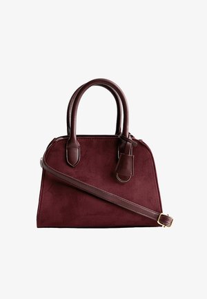 Burgundy suede handbag with structured shape, dual top handles, and a removable shoulder strap. Features a small attached leather tag.