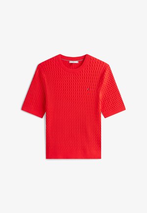 Punainen lyhythihainen neulepusero, jossa on tekstuuri- ja kuviointi sekä pieni logo vasemmassa rinnassa pyöreällä pääntiellä.