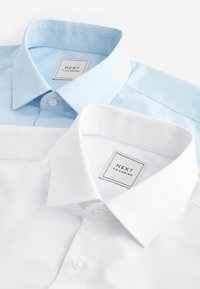 Zwei klassisch geschnittene Hemden mit Kragen: eines hellblau und das andere weiß. Beide haben Knopfverschlüsse und das Etikett "NEXT TAILORING" ist sichtbar.