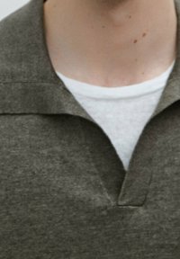 Donkergroen polo t-shirt met een gestructureerde afwerking, voorzien van een tweeknoopssluiting en een wit onderhemd dat daaronder zichtbaar is.