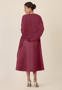 Burgundy dress with a flowing design, long sleeves, and a lightweight wrap. The skirt falls below the knee, paired with silver heeled sandals.