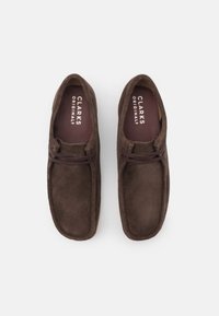 Chaussures beige en daim à enfiler avec une texture lisse, un bout arrondi et des détails de lacets décoratifs. Présente une semelle intérieure avec un logo.