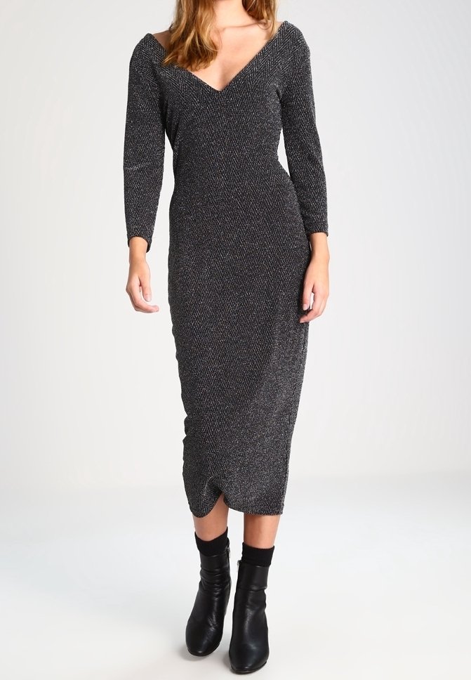 Robe midi à chevrons noire avec manches longues, décolleté en V et coupe près du corps. Portée avec des bottes à mi-mollet noires.
