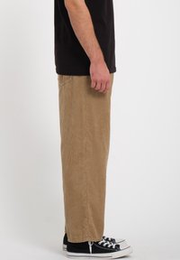 Lysebrune fløjlspants med lige ben, tekstureret ribbing, sidelommer, båret med sorte sneakers.
