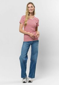 Sarkans un balts svītrainais īsām piedurknēm t-krekls ar apaļu kakla izgriezumu, kombinēts ar platām zilām džinsu biksēm un sudraba sporta apaviem.