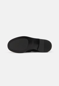 Black shoe sole with a smooth, flat surface and slight texture. Features a rounded toe and a tapered heel for stability.