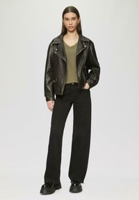 Zwarte leren motorjack met zilverkleurige hardware, gedragen over een olijfgroen V-halsshirt. Gepaard met hoge taille zwarte wijde broek en chunky zwarte schoenen.