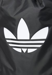 Tecido preto com uma textura suave apresenta um logo branco proeminente que se assemelha a três pétalas e três riscas horizontais.