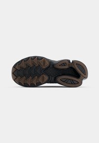 Sola di scarpa sportiva nera con una presa strutturata, dotata di una base in gomma e un motivo a tasselli triangolari. Accenti marroni evidenziano il design.