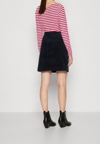 Camisa de manga larga a rayas con rayas rojas y blancas, combinada con una falda de pana azul marino con bolsillos traseros y botas de tacón negras hasta el tobillo.